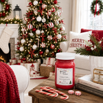 Load image into Gallery viewer, A red holiday-themed jar candle labeled 'Candy Cane' by Southern Charm Farmhouse sits on a wooden table in a cozy living room decorated for Christmas, with a lit tree, stockings, and candy canes nearby.

