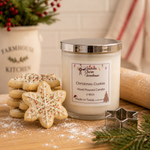 Load image into Gallery viewer, A hand-poured candle in a clear glass jar with a silver lid sits on a wooden table decorated for Christmas, surrounded by decorated sugar cookies, a metal star-shaped cookie cutter, and holiday greenery. The label reads 'Christmas Cookie'. Southern Charm Farmhouse.
