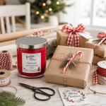 Load image into Gallery viewer, A red hand-poured candle in a clear glass jar with a silver lid and a white label reading 'Candy Cane' and 'Hand Poured Candle' is styled on a rustic white table with wrapped brown paper gifts, red-and-white gingham ribbons, spools of ribbon, scissors, pine branches, and a 'Merry Christmas' card. A blurred holiday tree and room background create a festive setting. Southern Charm Farmhouse.
