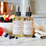 Load image into Gallery viewer, One room spray bottle and one Linen Spray bottle labeled 'Apple Berry Harvest' and 'Mulled Cider Press' on a surface with fruits and a towel.  Southern Charm Farmhouse.
