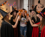Load image into Gallery viewer, Group of people in Halloween costumes and one wearing a Drink Up Witches T Shirt with black cape  celebrating with drinks in a decorated room. Southern Charm Farmhouse.
