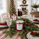 Load image into Gallery viewer, A red scented hand poured Home 4 the Holidays candle with a silver lid sits on a decorated Christmas table runner, surrounded by green pine branches, red napkins, and clear glassware in a festive dining room setting. Southern Charm Farmhouse.

