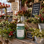 Load image into Gallery viewer, A green hand-painted Mistletoe (type) candle in a white jar sits on a rustic wooden market table surrounded by holiday greenery, mistletoe, metal buckets, and signs, including one that reads 'Fresh Mistletoe'. Southern Charm Farmhouse.
