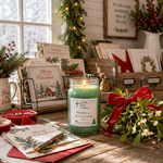 Load image into Gallery viewer, A lit green hand poured candle label reads Mistletoe (type) in a clear glass jar sits on a rustic wooden table surrounded by Christmas cards, greenery, red ribbon, and holiday decor in a warmly lit indoor setting. Southern Charm Farmhouse.
