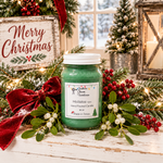 Load image into Gallery viewer, A green hand-poured Mistletoe (type) candle in a white jar sits on a rustic white wooden table surrounded by Christmas greenery, red berries, a red velvet bow, a 'Merry Christmas' sign, and a lantern in the background. Southern Charm Farmhouse.
