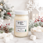 Load image into Gallery viewer, A hand-poured candle in a clear glass mason jar with a white lid, labeled 'Marshmallow Wonderland'. The jar is styled on a marble surface with marshmallows, pinecones, and frosted Christmas trees in the background. Southern Charm Farmhouse.
