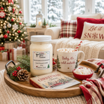 Load image into Gallery viewer, A cozy holiday living room scene with a wooden tray holding a hand poured jar candle labeled 'Marshmallow Wonderland' and a white mug that reads 'Baby, it's cold outside,' topped with marshmallows and a striped straw. A book, pinecones, berries, and a red plaid throw are arranged on the tray, with a Christmas tree, couch, and pillows in the background. Southern Charm Farmhouse.
