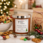Load image into Gallery viewer, A hand-poured candle in a clear glass jar with a silver lid and a white label reading ' Reindeer Munch,' styled on a tabletop with pretzels, candy, pine branches, and a kraft paper bag labeled 'Reindeer Munch' in a festive holiday setting. Southern Charm Farmhouse
