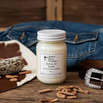 Load image into Gallery viewer, 16 oz mason Jar of Santal 33 candle with label on a wooden surface with denim, leather, and wicker elements. Southern Charm Farmhouse.
