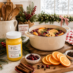 Load image into Gallery viewer, A jar of Spiced Holiday Cider hand-poured candle by Southern Charm Farmhouse sits on a wooden cutting board next to a large cream-colored pot filled with orange slices, cranberries, cinnamon sticks, and rosemary, with holiday decorations in the background.

