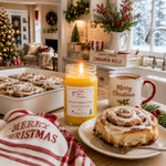 Load image into Gallery viewer, A lit yellow scented hand poured candle labeled Spiced Holiday Cider in a glass jar sits on a kitchen counter beside a cinnamon roll on a plate and a white mug that says Merry Christmas. A tray of cinnamon rolls, a red-and-white striped towel, and holiday decorations are visible in a warm, decorated kitchen setting. Southern Charm Farmhouse.
