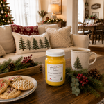 Load image into Gallery viewer, A holiday-themed hand-poured candle in a clear glass jar with a white lid sits on a wooden table in a cozy living room setting. The candle is labeled 'Spiced Holiday Cider' by Southern Charm Farmhouse.
