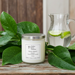 Load image into Gallery viewer, Hand poured 2 Wick Candle with a Storm Watch label on a wooden surface surrounded by green leaves and a glass pitcher with lime slices. Southern Charm Farmhouse.
