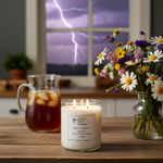 Load image into Gallery viewer, 2 Wick hand poured Candle with a storm-themed label on a table with a pitcher of iced tea and a vase of flowers, with a window showing lightning outside. Southern Charm Farmhouse
