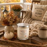 Load image into Gallery viewer, A jar hand poured candle labeled Vanilla Maple Pecan sits on a rustic wooden tray on a porch, styled with dried flowers in a vase, a small pumpkin, a mug, a chunky knit blanket, and a pillow that reads 'WELCOME TO OUR HOME'. Southern Charm Farmhouse.
