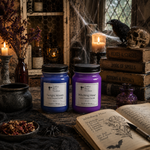 Load image into Gallery viewer, Two scented candles in glass jars, one blue and one purple, displayed on a rustic table surrounded by Halloween-themed props including a skull, a black raven, candles, an open notebook, and old books. Southern Charm Farmhouse
